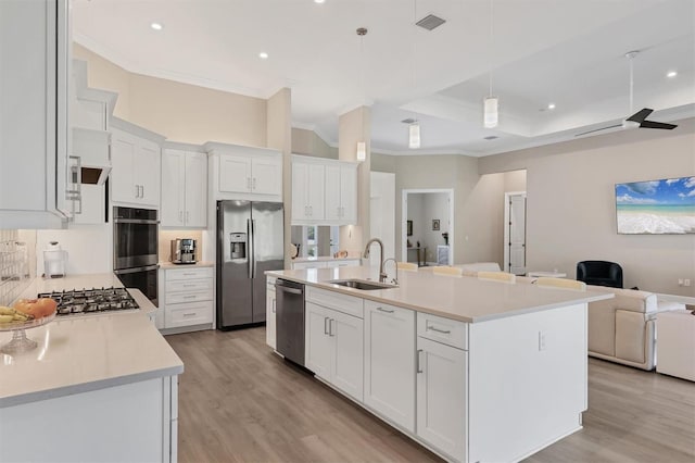 kitchen with stainless steel appliances, open floor plan, ornamental molding, a sink, and light wood finished floors