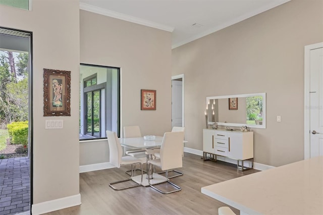 dining space featuring wood finished floors, plenty of natural light, crown molding, baseboards, and a towering ceiling