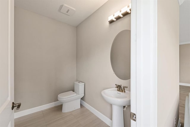half bath featuring toilet, a sink, and baseboards
