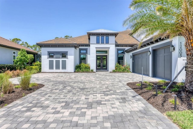 view of front of home with french doors, stucco siding, decorative driveway, a tiled roof, and an attached garage