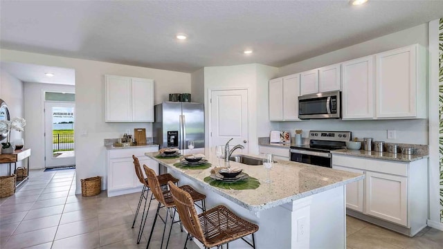 kitchen with stainless steel appliances, a sink, an island with sink, a breakfast bar area, and white cabinets