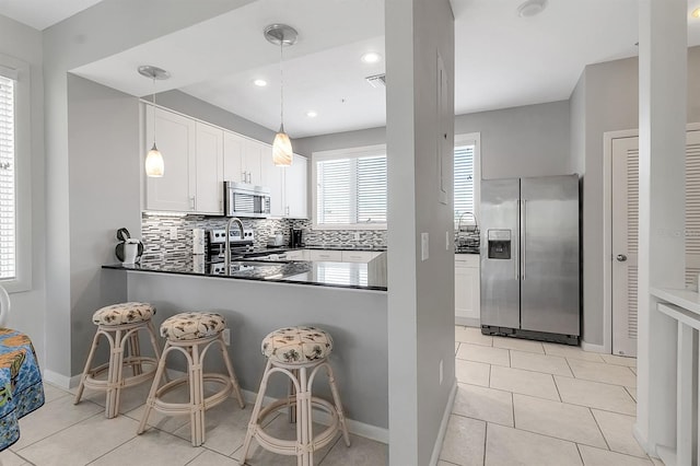 603 Cedars Ct, Longboat Key, FL 34228 - kitchen featuring appliances with stainless steel finishes, dark countertops, backsplash, a peninsula, and hanging light fixtures