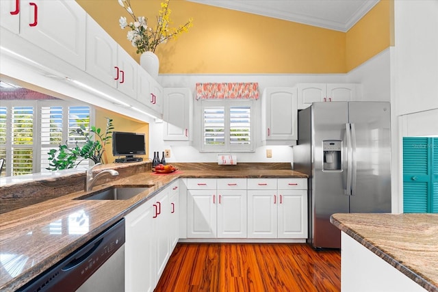 kitchen featuring appliances with stainless steel finishes, ornamental molding, a sink, white cabinets, and dark stone countertops