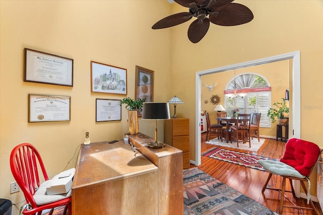 home office with wood finished floors, a towering ceiling, and ceiling fan