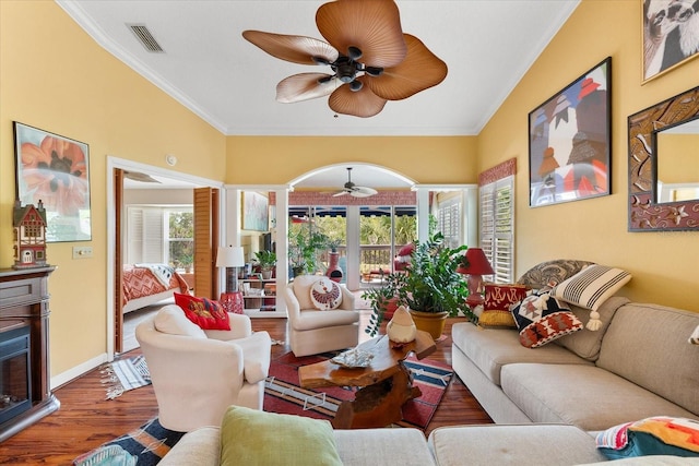 living room featuring ceiling fan, wood finished floors, ornamental molding, and a fireplace with raised hearth