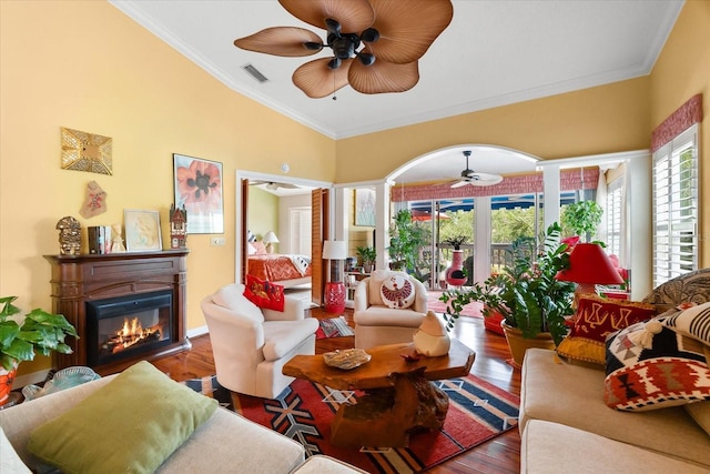 living area featuring ceiling fan, a glass covered fireplace, healthy amount of natural light, wood finished floors, and ornamental molding