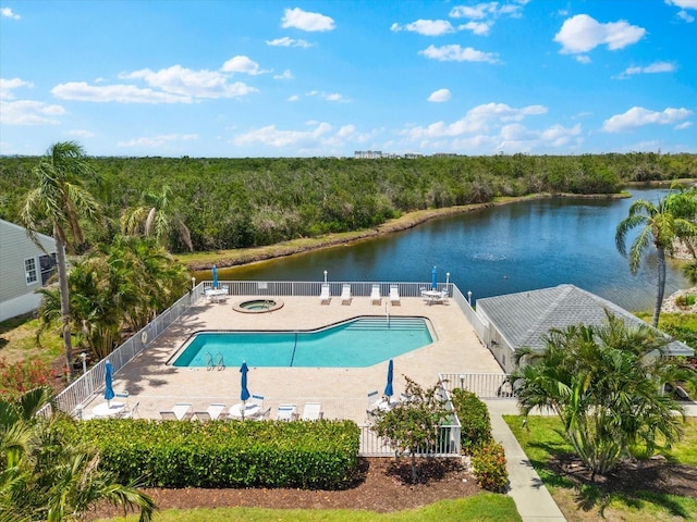 community pool featuring fence, a water view, a wooded view, a patio area, and a hot tub