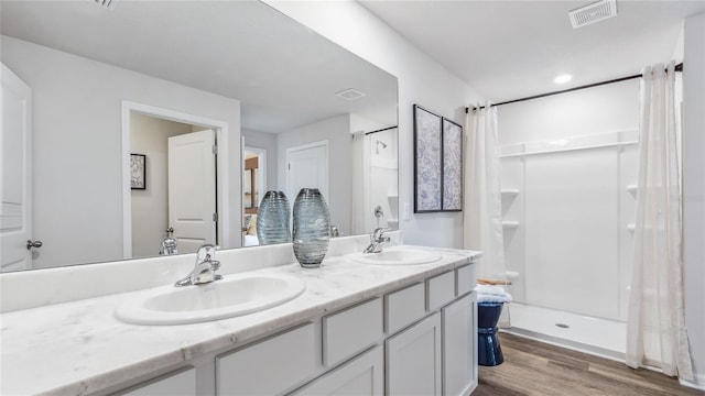 full bath featuring wood finished floors, a shower stall, and double vanity