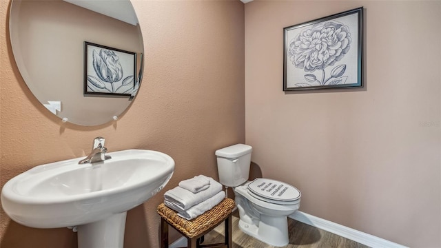 half bath with toilet, wood finished floors, a sink, and baseboards