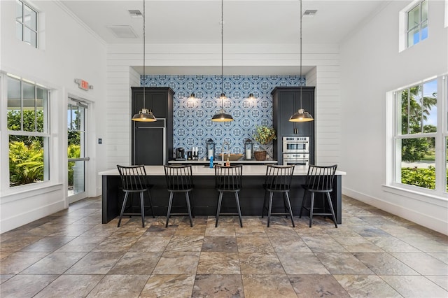 13708 Old Creek Ct, Parrish, FL 34219 - kitchen with crown molding, an accent wall, light stone finish flooring, an island with sink, and baseboards