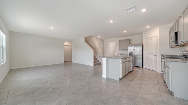12728 Lateral Root Dr, Sarasota, FL 34238 - kitchen with arched walkways, stainless steel appliances, gray cabinets, a sink, and a kitchen island with sink