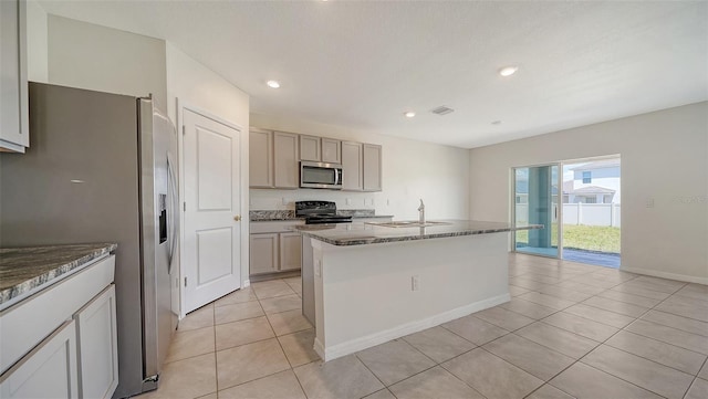 12732 Lateral Root Dr, Sarasota, FL 34238 - kitchen with stainless steel appliances, light tile patterned flooring, dark stone countertops, a sink, and an island with sink
