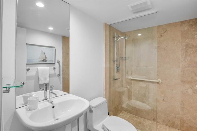 bathroom with a tile shower, toilet, a sink, and recessed lighting