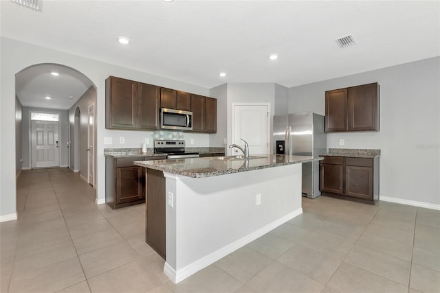 12712 Dusty Trail Dr, Sarasota, FL 34238 - kitchen featuring stainless steel appliances, a sink, arched walkways, stone counters, and dark brown cabinets