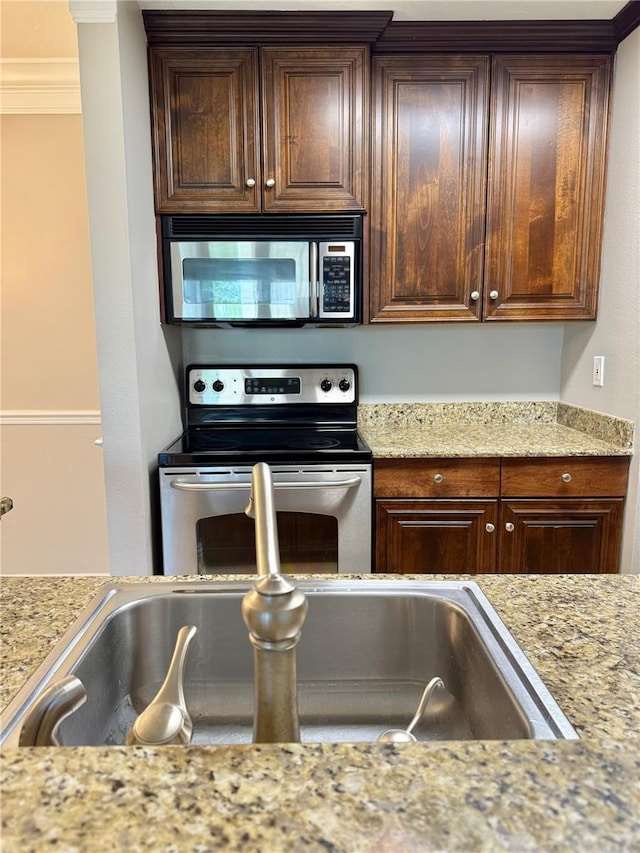 4037 Crockers Lake Blvd Unit 14, Sarasota, FL 34238 - kitchen with appliances with stainless steel finishes, ornamental molding, light stone countertops, dark brown cabinetry, and a sink
