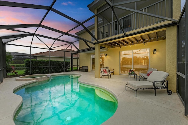 pool at dusk with a patio, a pool with connected hot tub, and glass enclosure