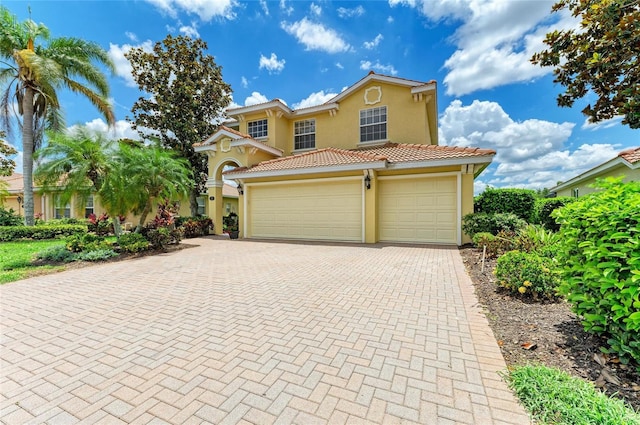 mediterranean / spanish-style home featuring stucco siding, decorative driveway, a tiled roof, and a garage