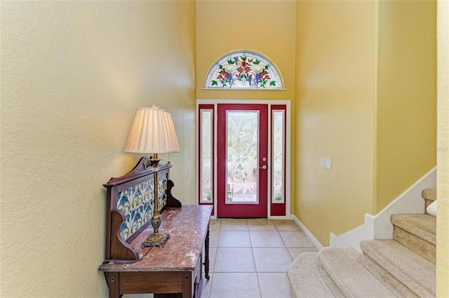 tiled entrance foyer featuring a towering ceiling, a textured wall, baseboards, and stairway