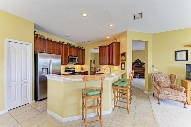 kitchen featuring stainless steel appliances, a peninsula, light countertops, a breakfast bar area, and light tile patterned floors