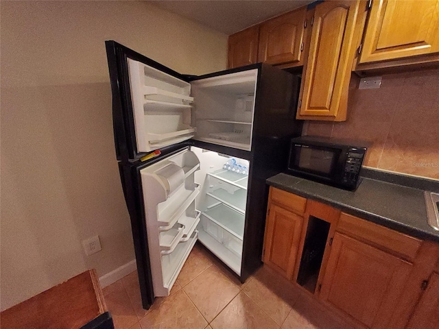 4607 W N B St Unit 105, Tampa, FL 33609 - kitchen with black microwave, freestanding refrigerator, light tile patterned floors, and brown cabinetry