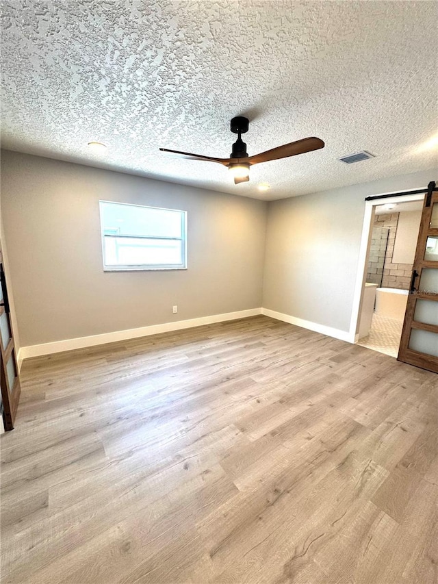 6524 Senegal Palm Way, Apollo Beach, FL 33572 - unfurnished room featuring ceiling fan, a barn door, wood finished floors, baseboards, and a textured ceiling