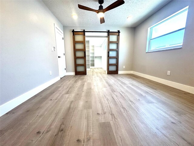 6524 Senegal Palm Way, Apollo Beach, FL 33572 - empty room featuring a barn door, a ceiling fan, wood finished floors, baseboards, and a textured ceiling