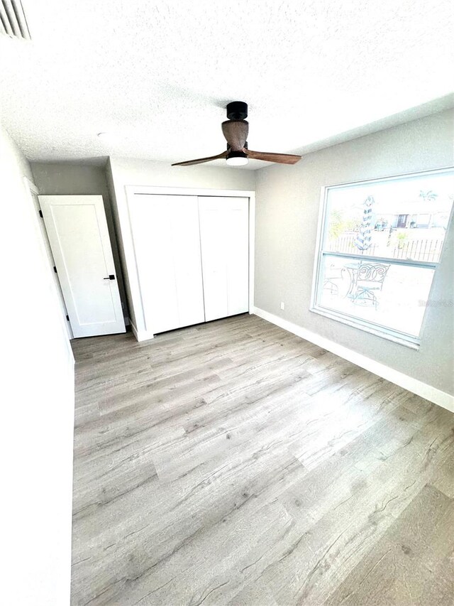 6524 Senegal Palm Way, Apollo Beach, FL 33572 - unfurnished bedroom with baseboards, a closet, light wood-style flooring, a textured ceiling, and a ceiling fan