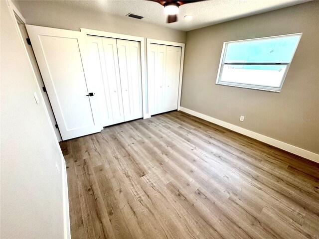 6524 Senegal Palm Way, Apollo Beach, FL 33572 - unfurnished bedroom with two closets, baseboards, wood finished floors, a textured ceiling, and a ceiling fan
