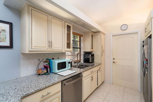 kitchen featuring cream cabinets, appliances with stainless steel finishes, a sink, backsplash, and light stone counters