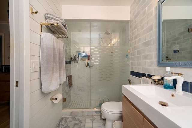 bathroom with tile walls, a shower stall, toilet, vanity, and tile patterned floors
