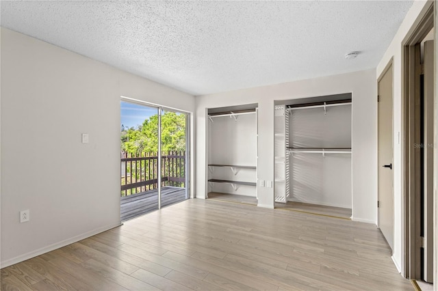 3212 Ramblewood Dr N Unit 3212, Sarasota, FL 34237 - unfurnished bedroom with two closets, access to outside, a textured ceiling, light wood finished floors, and baseboards