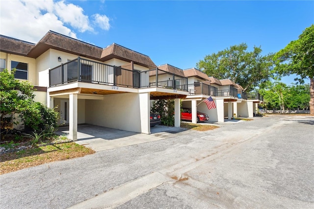 3212 Ramblewood Dr N Unit 3212, Sarasota, FL 34237 - view of front facade with mansard roof, stucco siding, a carport, a shingled roof, and a balcony