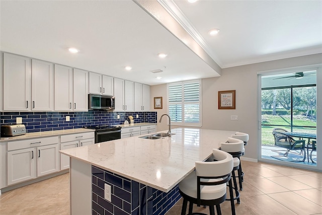 1017 Tidewater Shores Loop Unit 1017, Bradenton, FL 34208 - kitchen featuring a sink, stainless steel microwave, black range with electric cooktop, backsplash, and a center island with sink