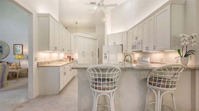 4208 Balmoral Way, Sarasota, FL 34238 - kitchen featuring white appliances, a peninsula, a kitchen bar, light stone countertops, and a high ceiling