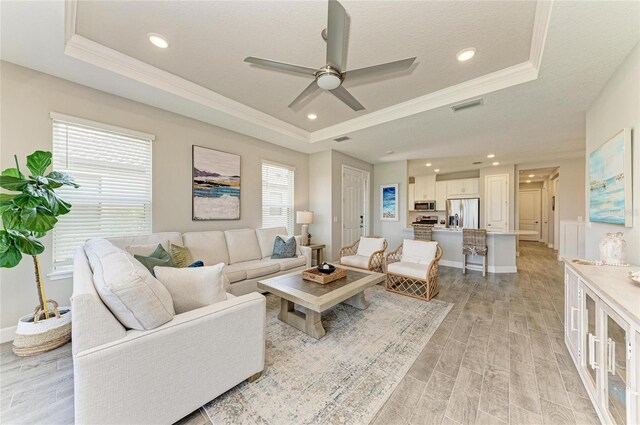 3027 Formia Ct, Lakewood Ranch, FL 34211 - living area with a tray ceiling, a ceiling fan, ornamental molding, light wood-style floors, and recessed lighting