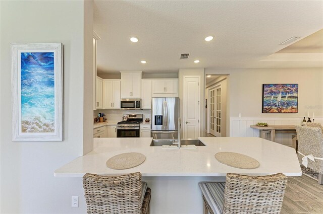 3027 Formia Ct, Lakewood Ranch, FL 34211 - kitchen featuring appliances with stainless steel finishes, a kitchen bar, light countertops, white cabinets, and light wood finished floors