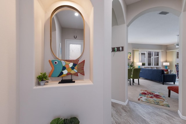 hallway with arched walkways, wood finished floors, and baseboards