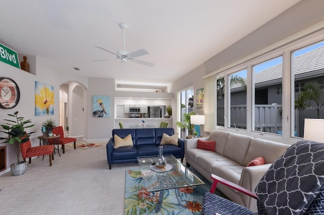 carpeted living room with arched walkways, ceiling fan, and baseboards