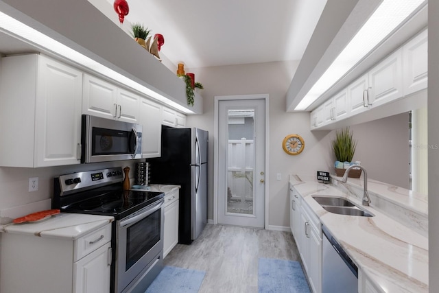 kitchen with appliances with stainless steel finishes, a sink, light wood-style floors, white cabinets, and baseboards