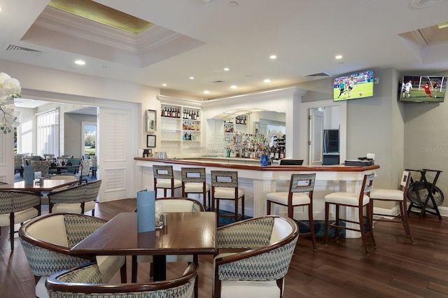 dining space featuring ornamental molding, recessed lighting, a raised ceiling, wood finished floors, and a community bar