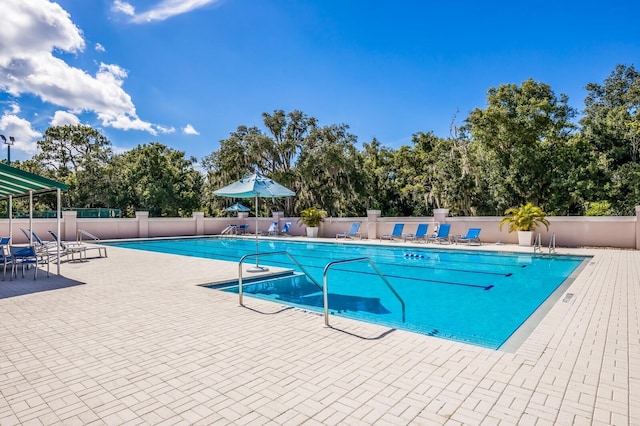 community pool featuring fence, a patio area, and view of wooded area