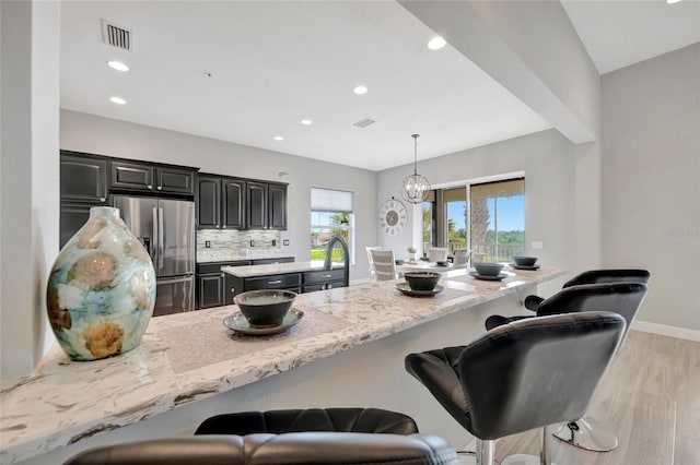 23233 Banbury Way Unit 302, Venice, FL 34293 - kitchen with stainless steel fridge with ice dispenser, a center island, a kitchen bar, light wood-type flooring, and recessed lighting