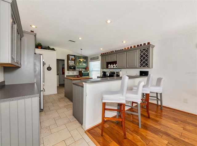 230 Fareham Dr, Venice, FL 34293 - kitchen with freestanding refrigerator, a kitchen bar, lofted ceiling, gray cabinetry, and dark countertops