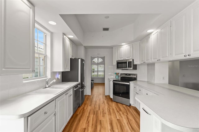 7716 Uliva Way, Sarasota, FL 34238 - kitchen with stainless steel appliances, a sink, white cabinetry, light wood finished floors, and light countertops