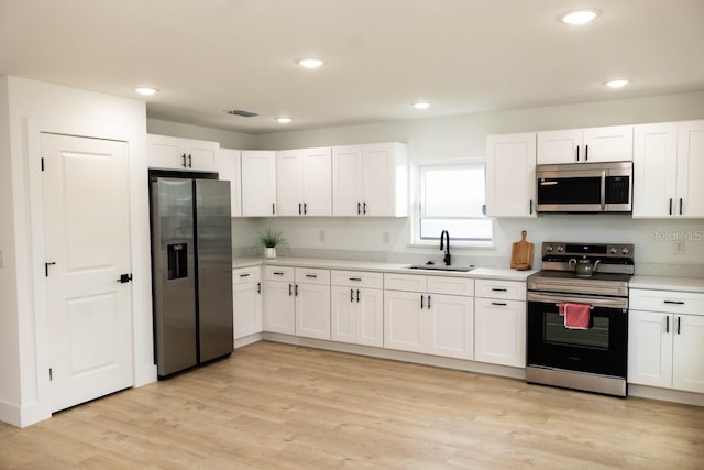 kitchen with stainless steel appliances, a sink, light countertops, white cabinets, and recessed lighting