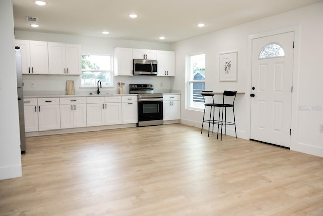 kitchen with stainless steel appliances, a sink, white cabinets, light wood-type flooring, and light countertops