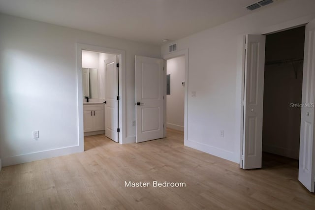 unfurnished bedroom featuring light wood-style floors, baseboards, and a walk in closet