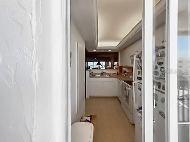8977 Midnight Pass Rd Unit 521, Sarasota, FL 34242 - kitchen featuring white range with electric stovetop, a sink, white cabinetry, light tile patterned floors, and a raised ceiling