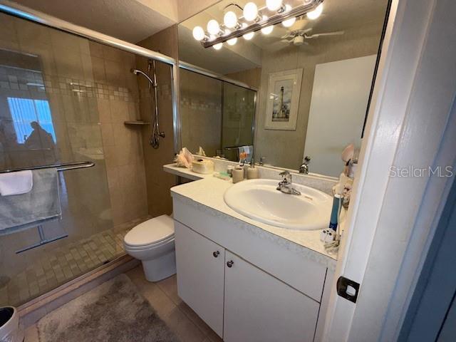 8977 Midnight Pass Rd Unit 521, Sarasota, FL 34242 - bathroom with vanity, toilet, a stall shower, tile patterned floors, and a ceiling fan