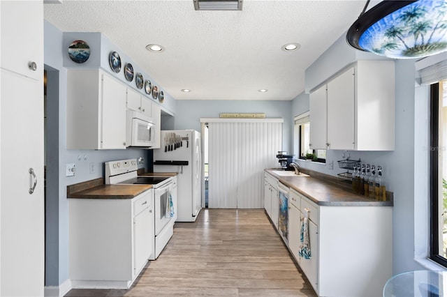 4203 Carriage Dr Unit 27, Sarasota, FL 34241 - kitchen featuring white appliances, a sink, dark countertops, light wood-style flooring, and white cabinets